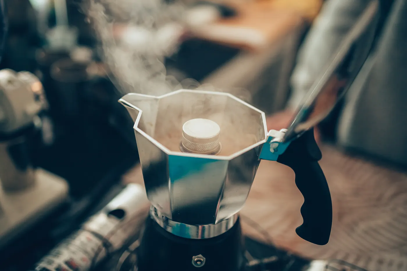 A stovetop moka pot brewing espresso-style coffee on a gas burner beside a small cup