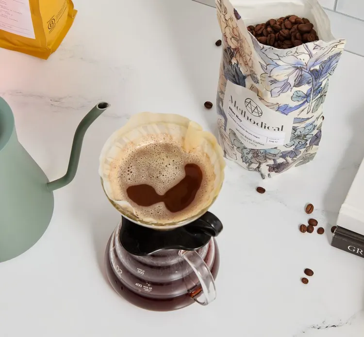 A pour-over brewing on a marble counter beside a Fellow kettle and a bag of freshly roasted coffee